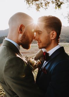 two men standing next to each other in front of a tree with the sun shining on them