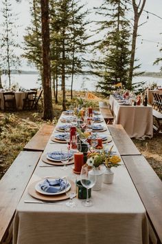 a long table set up with plates and place settings for an outdoor dinner by the water