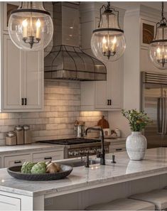 a large kitchen with white cabinets and marble counter tops, hanging lights over the island