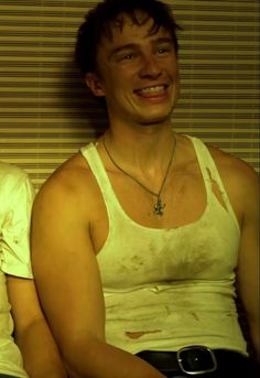 two young men sitting next to each other in front of a wall with blinds on it