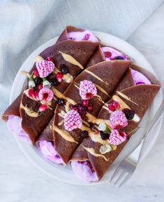 a white plate topped with chocolate crepes covered in fruit and drizzle