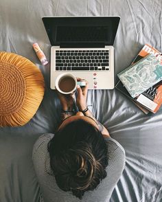 a person sitting on a bed with a laptop and coffee in front of their head