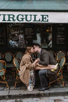 a man and woman kissing in front of a cafe with chairs on the side walk