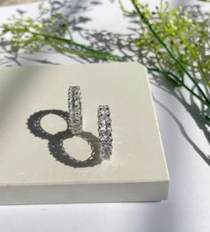 a pair of diamond hoop earrings sitting on top of a white box next to flowers