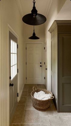 an empty hallway with a basket on the floor and two lights hanging from the ceiling