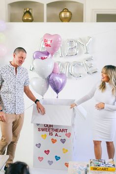 a man and woman standing in front of a baby shower sign with balloons on it