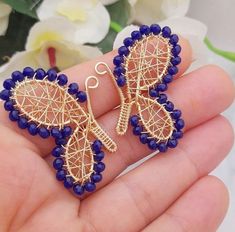 a pair of earrings with blue beads and gold filigrees in the shape of butterfly wings