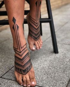 a woman's legs with tattoos on them sitting in front of a chair and looking at the ground