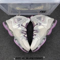 a pair of white and purple sneakers in a clear box on the floor with black carpet