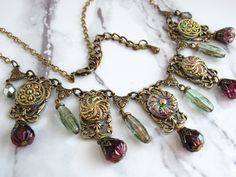 This statement necklace is made with gorgeous iridescent Czech glass buttons, Czech glass beads, and antiqued brass filigree, stampings, and chain. The buttons are iridescent purple and green with a metallic gold top finish. So much shine to these! The glass beads are translucent sage green with copper foil on the inside, and translucent purple.  The necklace secures with a lobster claw clasp and has a 2" chain extender. --Necklace length is 16.5" (not including chain extender or length of any b Upcycling Jewelry, Bijoux Art Nouveau, Purple Sage, Iridescent Purple, Brass Filigree, Goddess Necklace, Witchy Jewelry, Filigree Pendant, Art Nouveau Jewelry