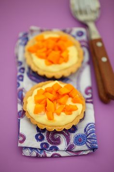 two small pies are sitting on a purple tablecloth with a spoon next to it