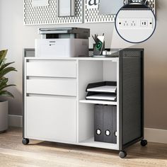 a white cabinet with drawers and some pictures on the wall next to it in front of a potted plant