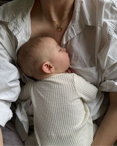 a woman holding a baby in her arms while wearing a white shirt and gold necklace