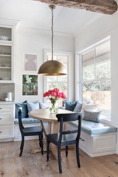 a dining room table with two chairs and a bench in front of the window that has flowers on it