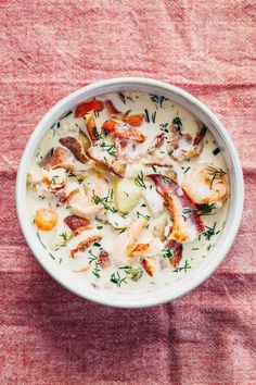 a white bowl filled with seafood chowder on top of a red cloth