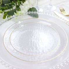 a white and gold table setting with flowers on the plate, silverware and napkins