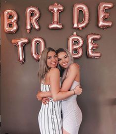 two women hugging each other in front of a sign that says bride to be on it