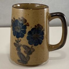 a coffee mug with blue flowers on it sitting on a white counter top next to a wall