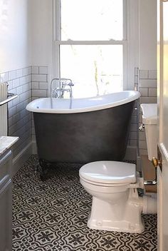 a bath tub sitting next to a white toilet in a bathroom with black and white flooring