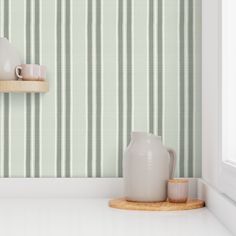 two white vases are sitting on a shelf in front of a green striped wallpaper