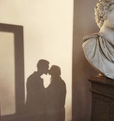 the shadow of two people kissing in front of a bust of a man and woman