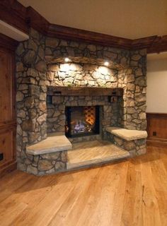 an empty room with a stone fireplace and wood floors in the center is lit by recessed lights