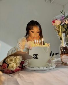 a woman sitting in front of a cake with lit candles on it and flowers behind her