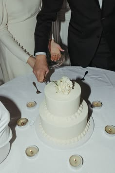 a man and woman cutting into a white cake on top of a table with candles