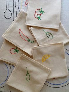 four embroidered napkins with fruit and vegetables on them