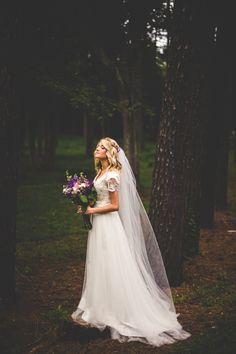 a woman in a wedding dress standing next to a tree with her veil pulled back