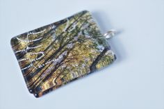 a square glass pendant with trees in the woods on it's side, sitting on a white surface