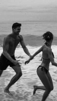 two people running in the water at the beach