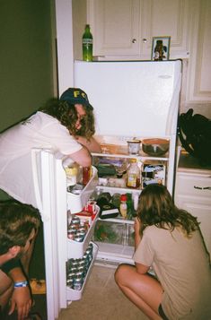 two people squatting down in front of an open refrigerator