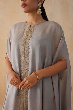 Grey kaftan with zari embroidered center front, attached fringes on hem and asymmetric hemline. Paired with a cream wide leg pant and an inner slip. - Aza Fashions Elegant Abaya With Dupatta, Elegant Eid Sets With Tassels, Elegant Embroidered Kurta With Cape Sleeves, Elegant Kurta With Zari Work And Cape Sleeves, Traditional Drape Abaya With Resham Embroidery, Elegant Tunic With Zari Work For Eid, Elegant Eid Tunic With Zari Work, Elegant Resham Embroidered Tunic Kaftan, Elegant Festive Kaftan With Embroidered Border