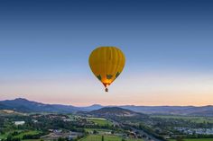 a yellow hot air balloon flying over a lush green valley under a clear blue sky