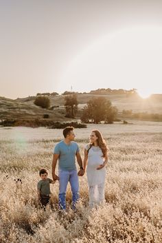 a man and woman holding hands while standing next to a small boy in a field