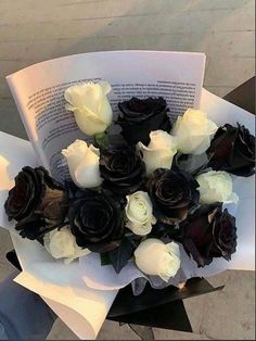 a bouquet of white and black roses sitting on top of an open book in someone's hand