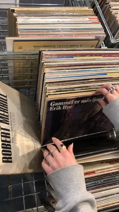 a woman is picking up records from a rack in a record store, with her hands on top of them