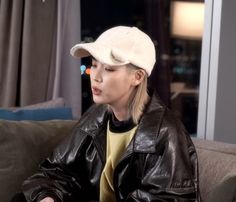 a woman sitting on top of a couch wearing a black leather jacket and white hat