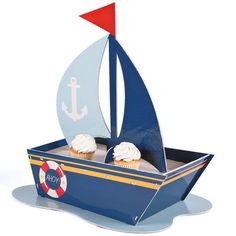 a cupcake in a box with a sailboat on it's side and two cupcakes inside