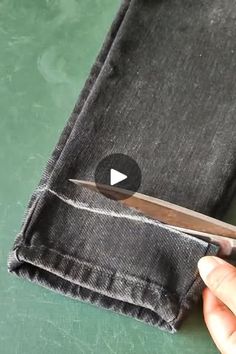 someone using scissors to cut the side of a pair of jeans