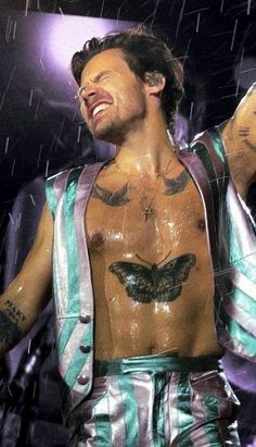 a man with tattoos on his chest standing in the rain