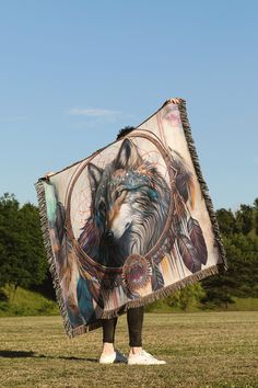 a person standing in a field holding a blanket with an image of a wolf on it