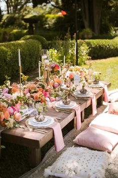 an outdoor table set up with pink and white flowers, candles, and place settings