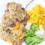 a white plate topped with broccoli, corn and meat next to a spoon