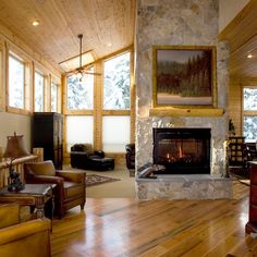 a large living room with wood floors and stone fireplace in the center surrounded by windows