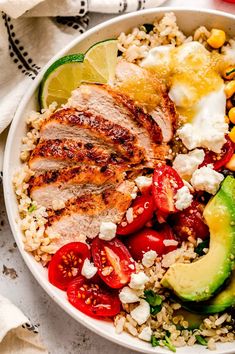 a white bowl filled with rice, meat and veggies next to sliced avocado