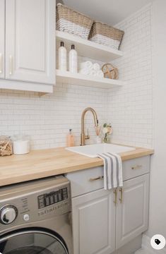 a washer and dryer in a small room with white cabinets, wood counter tops and open shelving