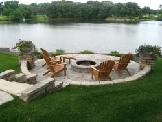 a fire pit surrounded by lawn chairs next to a lake