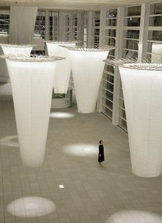 a woman is standing in the middle of a room with large white lamps hanging from the ceiling